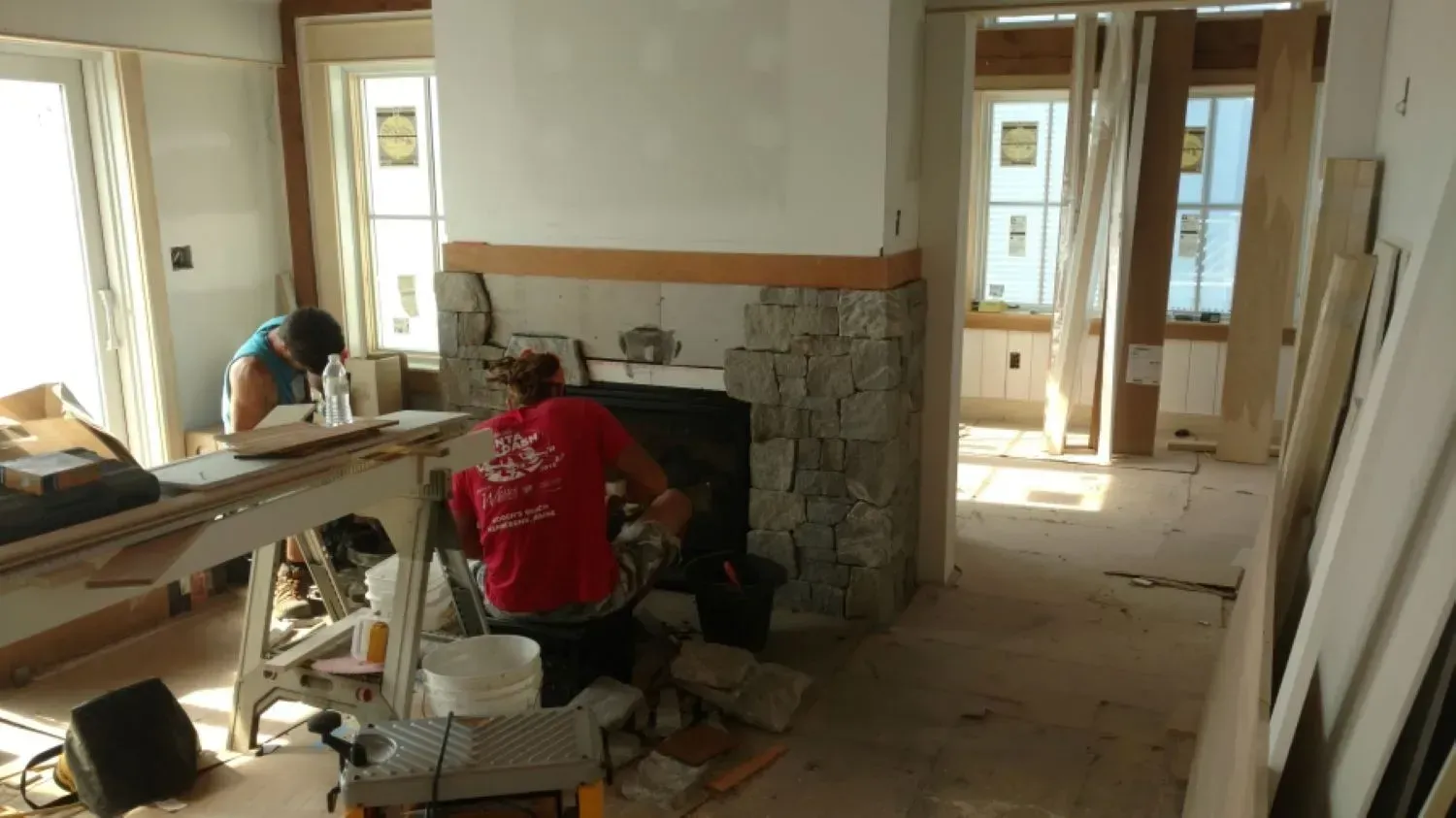 A man in a red shirt is working on a fireplace in a living room.