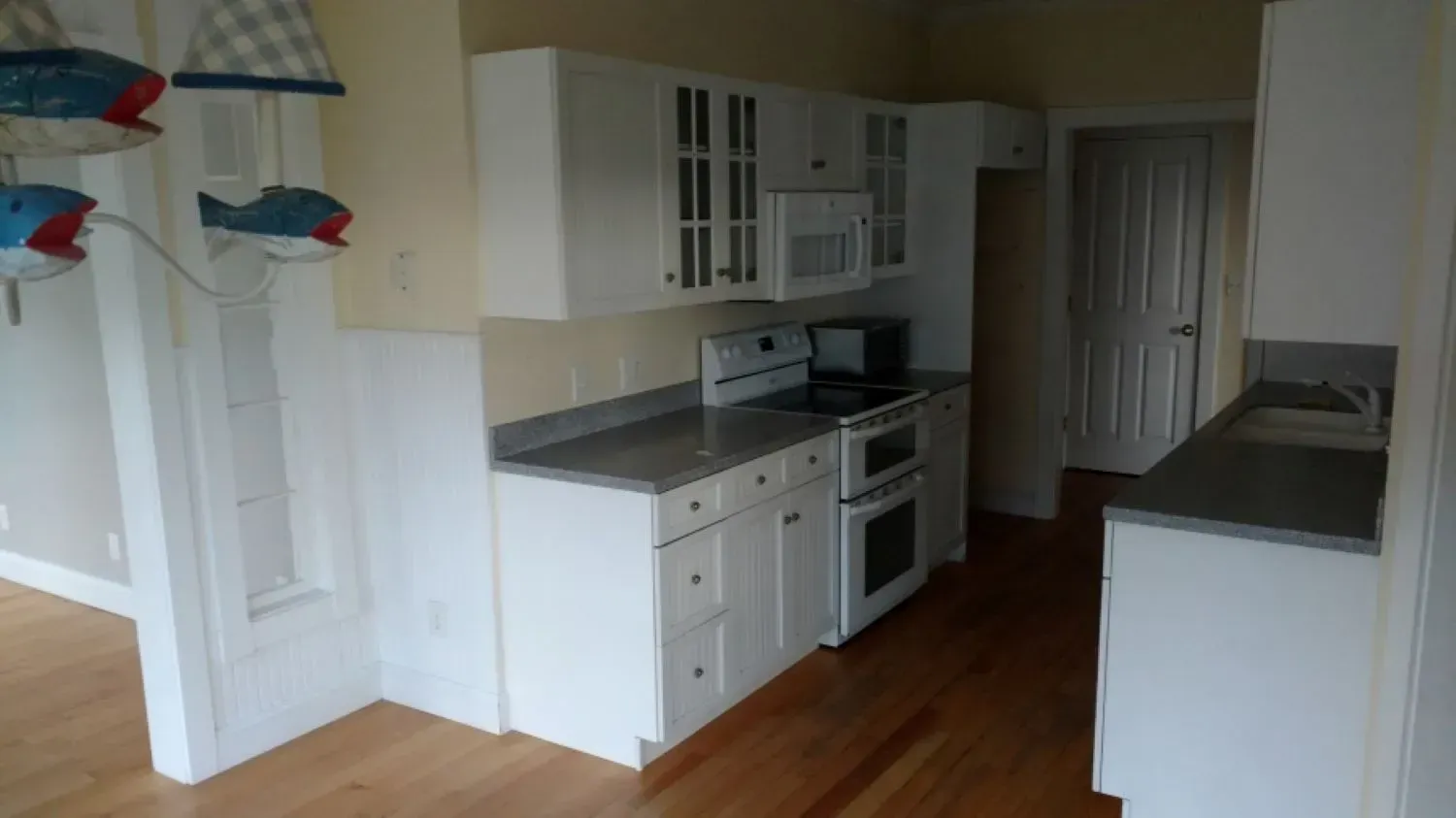 A kitchen with white cabinets , a stove , a microwave , and a sink.