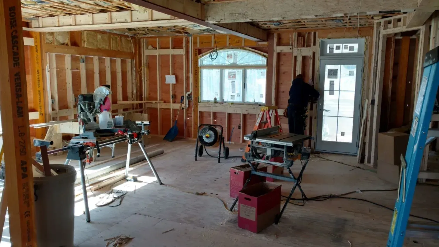A room in a house under construction with a table saw and a ladder.