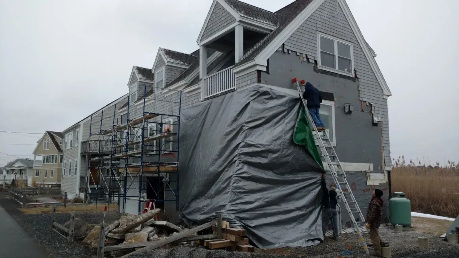 A house is being covered with a tarp and workers are working on it.