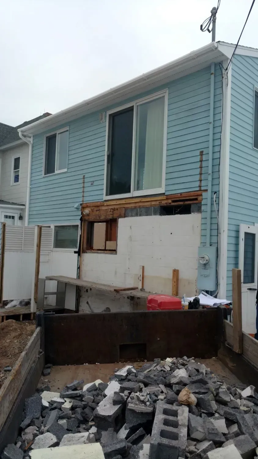 A blue house is being demolished with a pile of bricks in front of it.