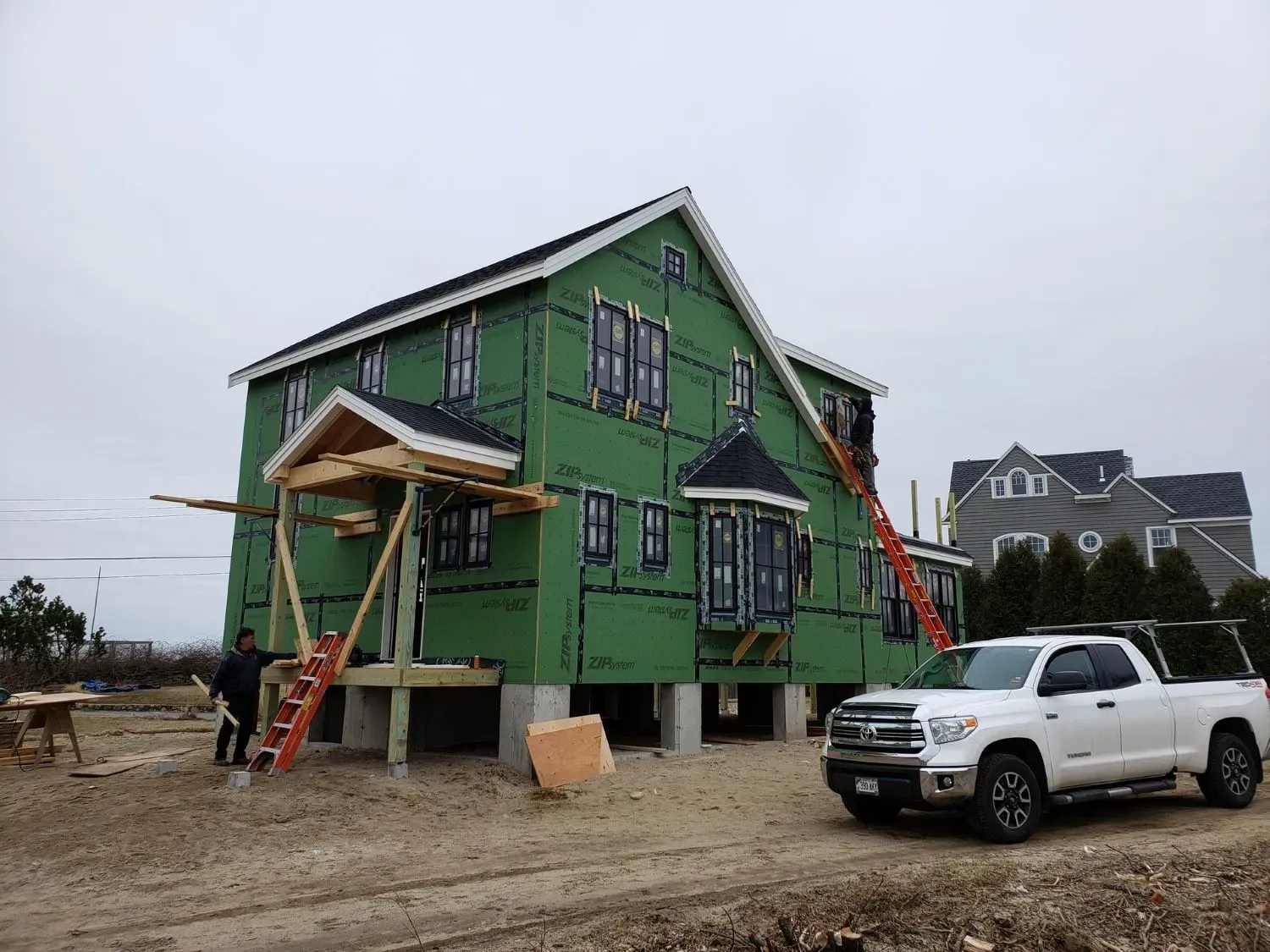 A white truck is parked in front of a house under construction.