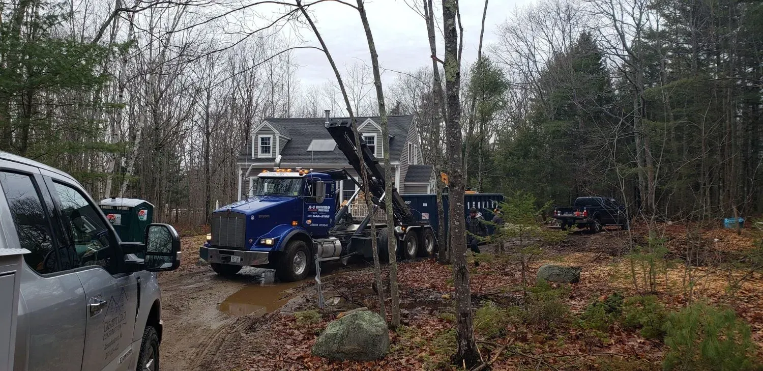 A truck is parked in front of a house in the woods.
