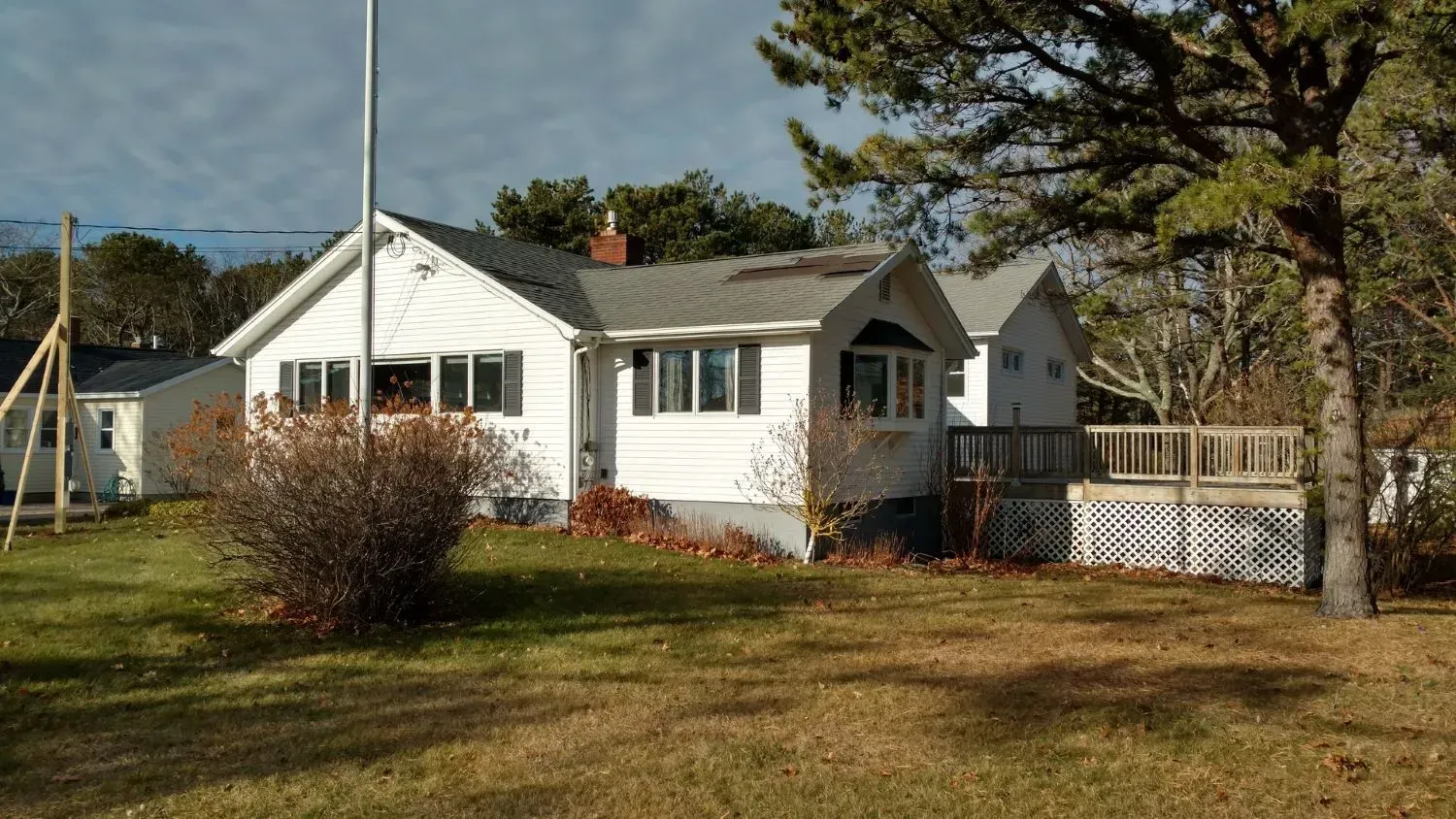 A white house with a gray roof is sitting in the middle of a grassy field.