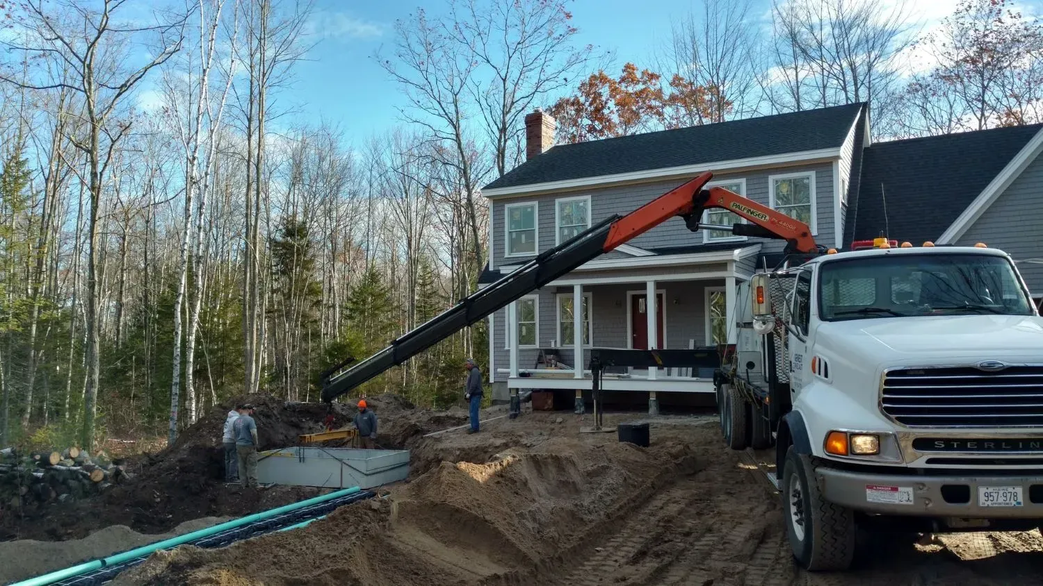 A white truck with a crane attached to it is parked in front of a house.