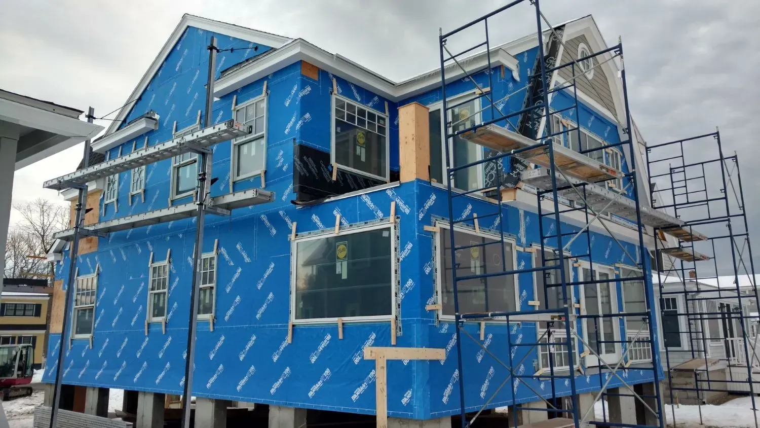 A large house is being built with blue siding and scaffolding.
