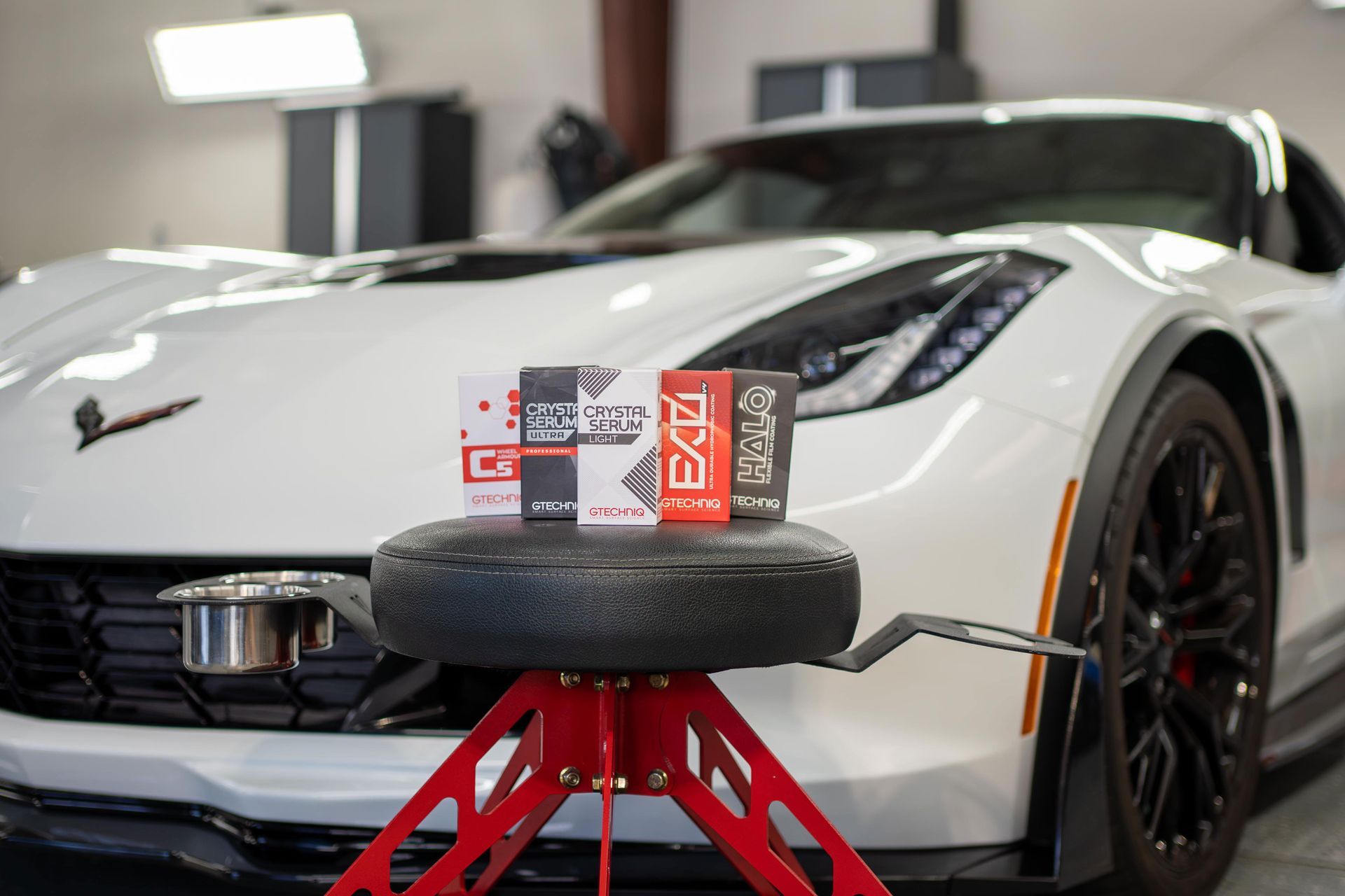 A white sports car is parked in a garage next to a red stool.