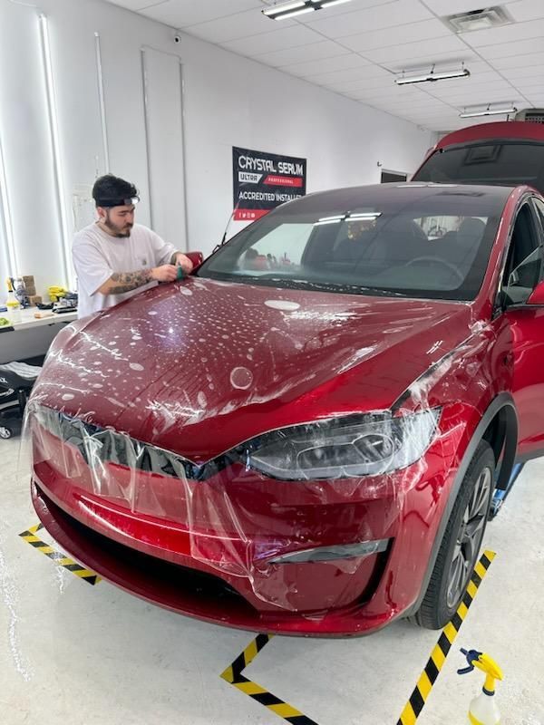 A man is wrapping a red tesla model x in plastic.