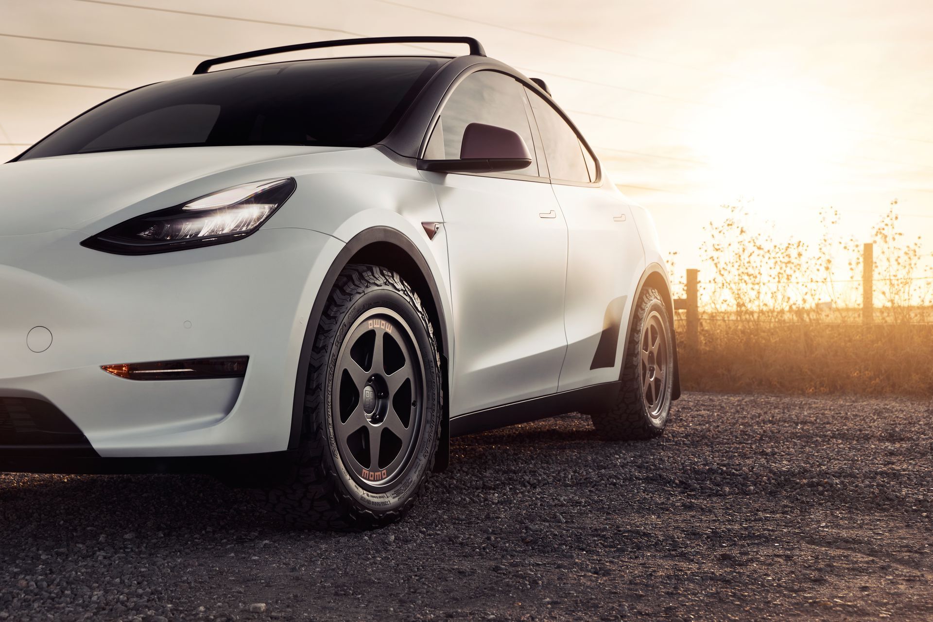 A white tesla model y is parked on a dirt road.