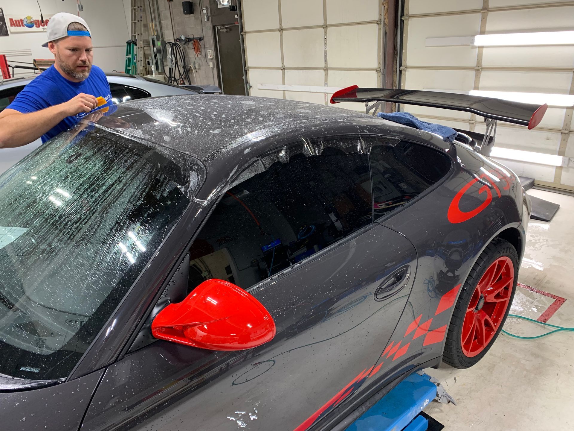 A man is wrapping the roof of a porsche 911 gt3 rs in plastic.