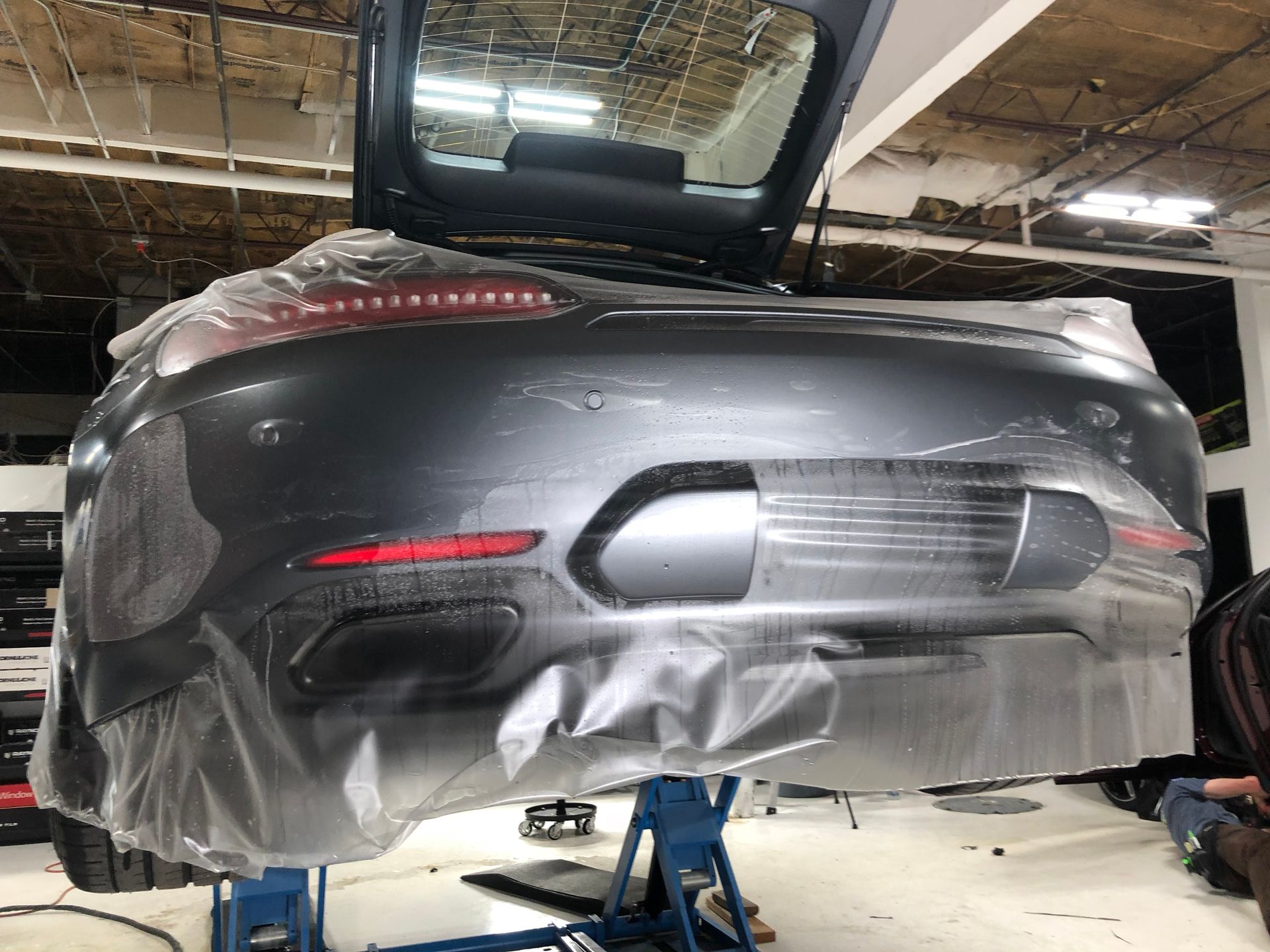 A car is wrapped in plastic and sitting on a lift in a garage.