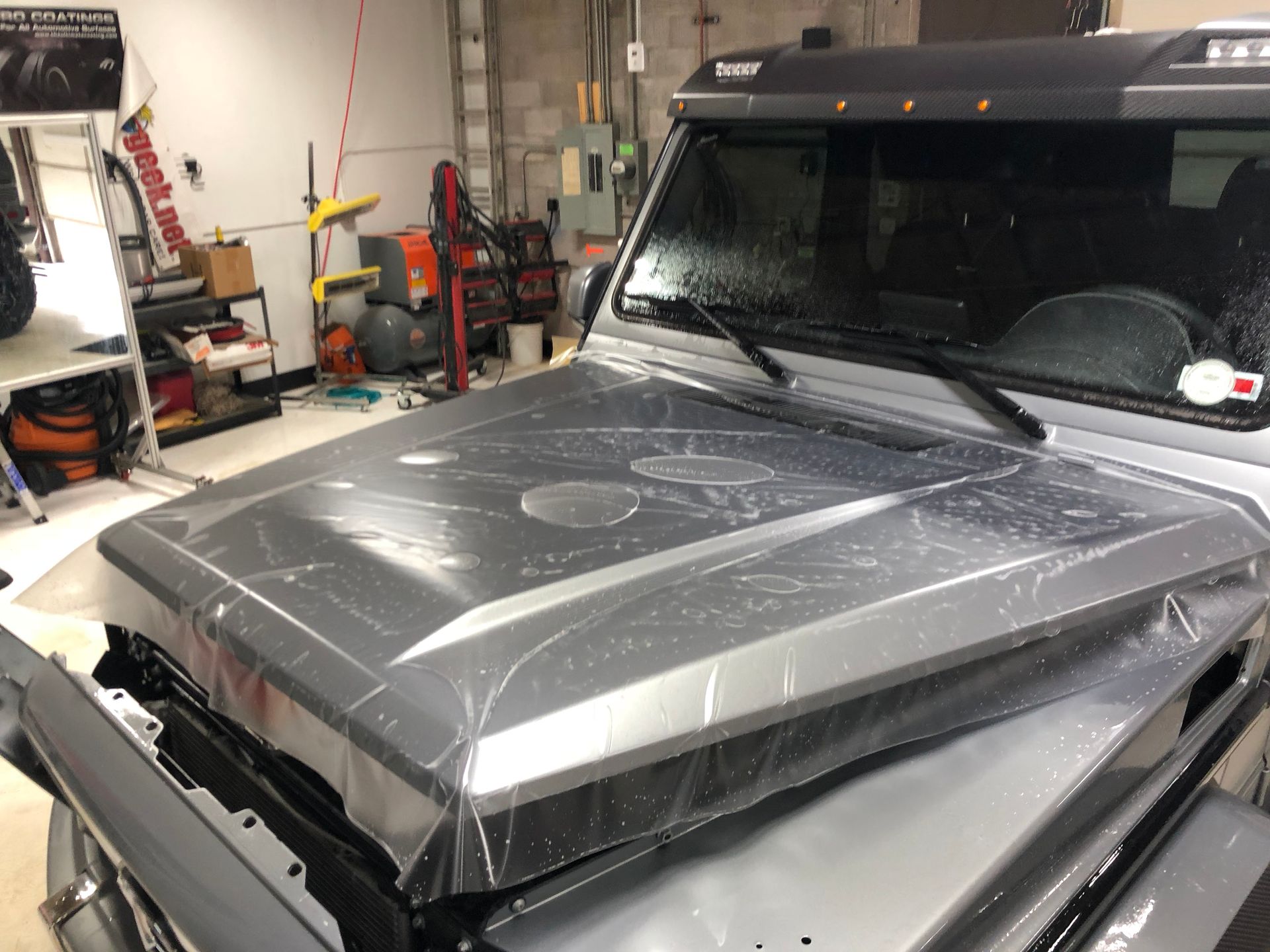 The hood of a jeep is wrapped in plastic in a garage.