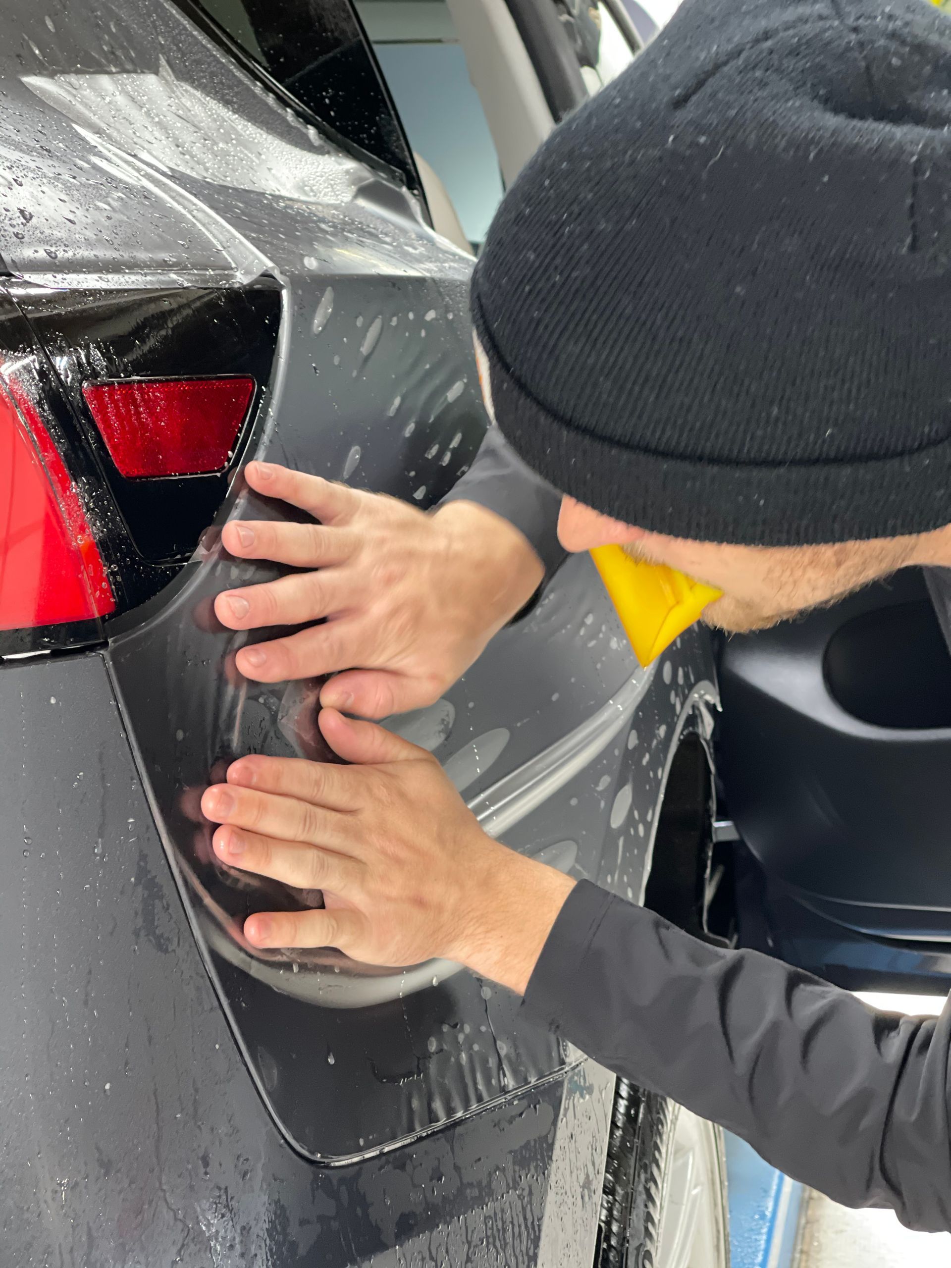 A man in a black hat is cleaning the back of a car