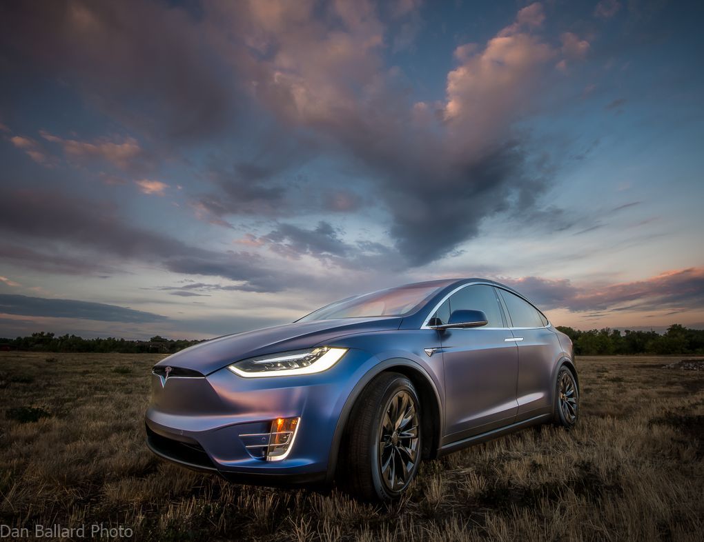 A blue tesla model x is parked in a field at sunset.