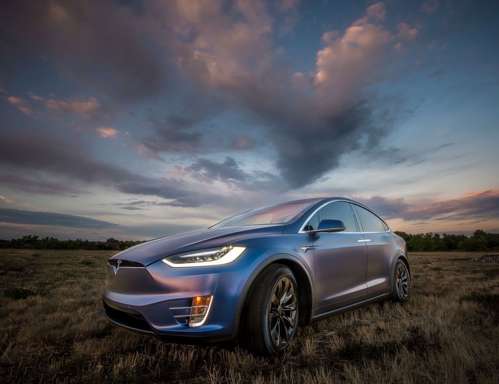 A blue tesla model x is parked in a field at sunset.