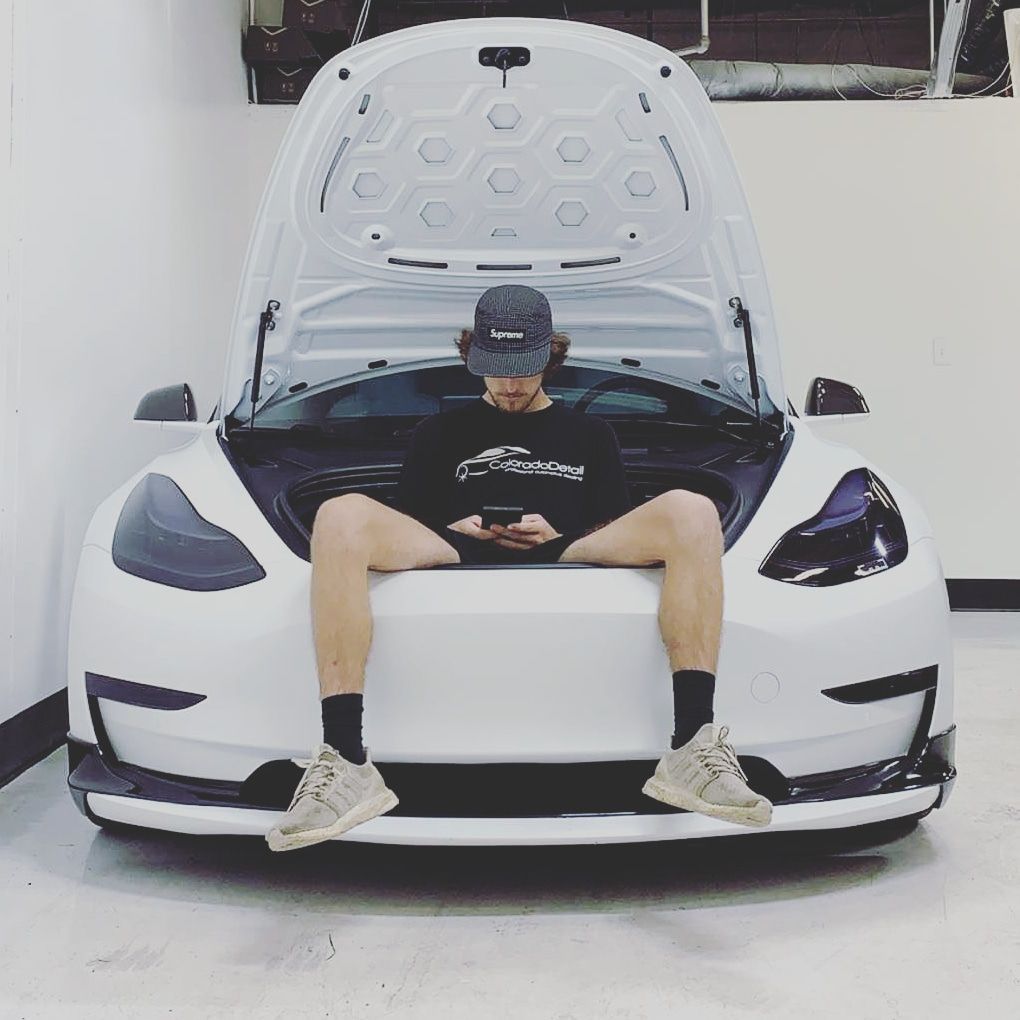 A man is sitting on the hood of a tesla model 3