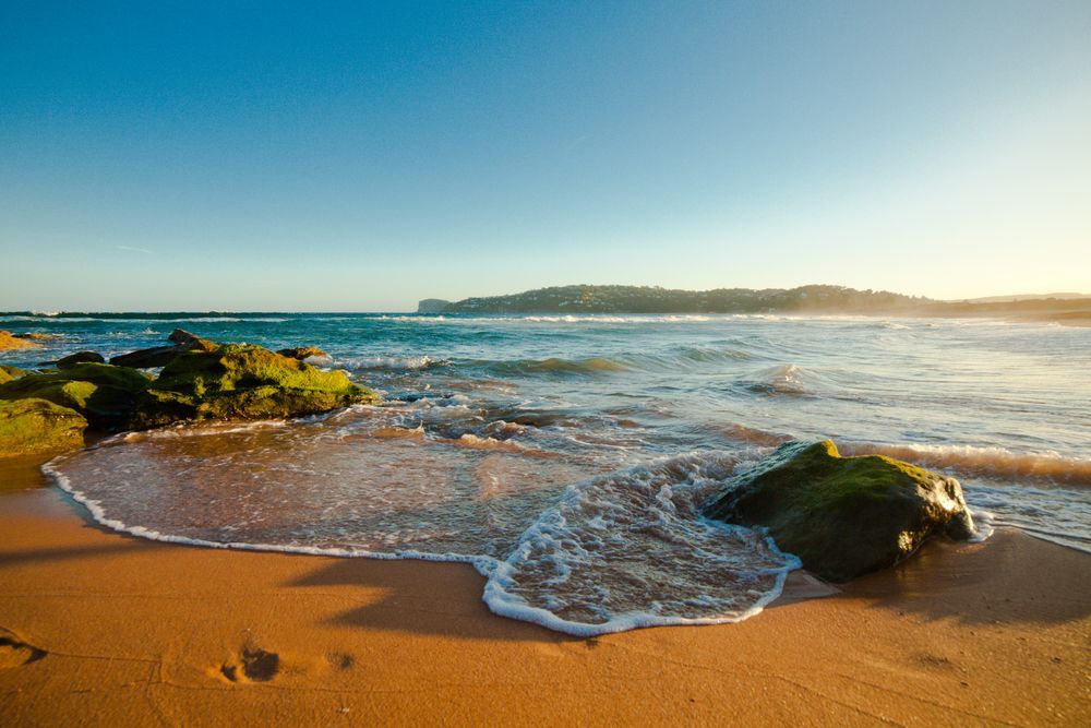 A Sandy Beach With Rocks And Waves Crashing On It — Hats Off Kitchens in Sydney Northern Beaches, NSW