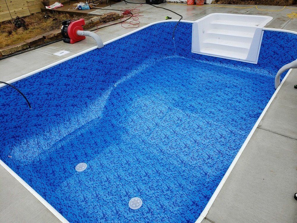 A blue swimming pool with white stairs is being built.