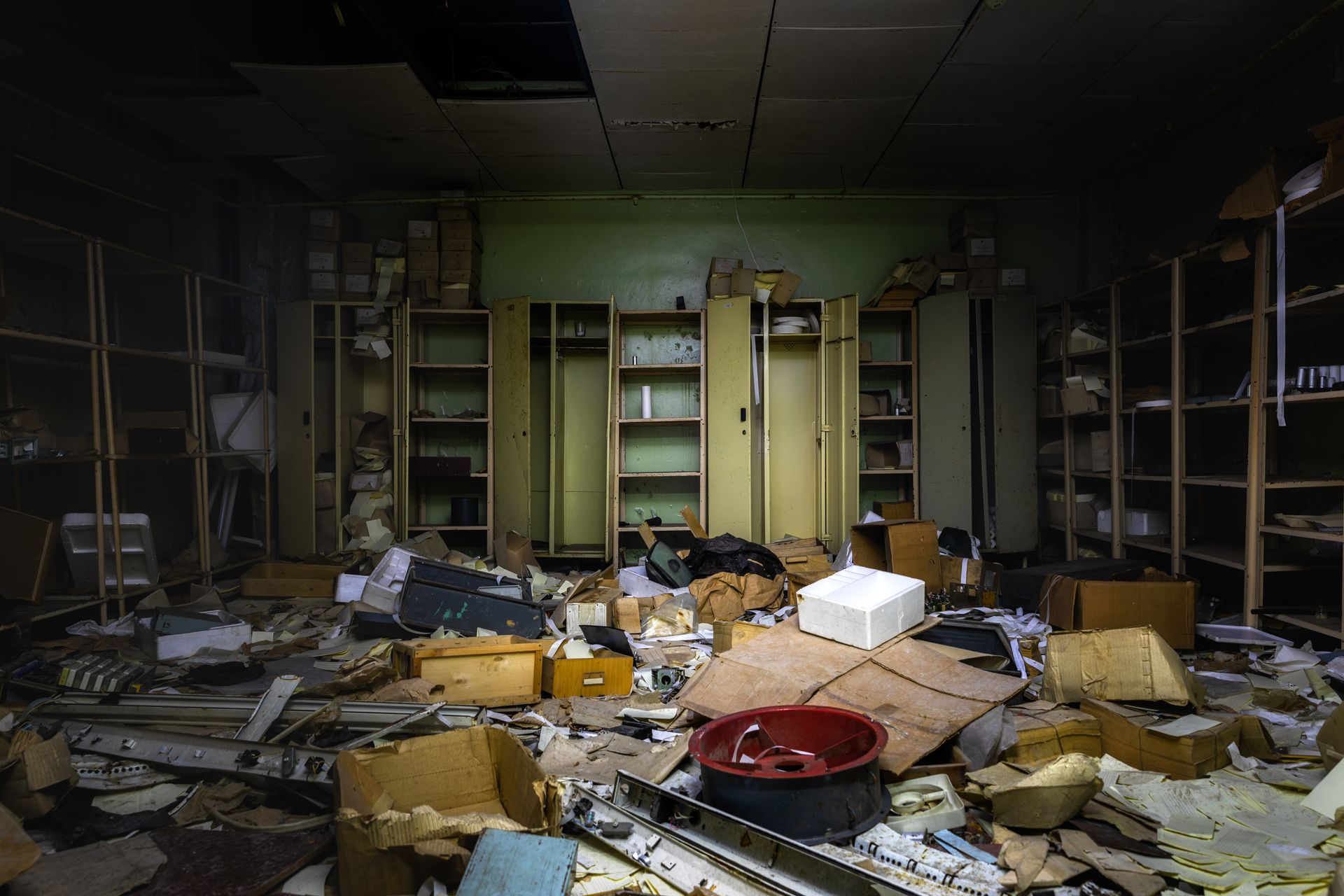 An abandoned room with a lot of boxes on the floor and shelves.