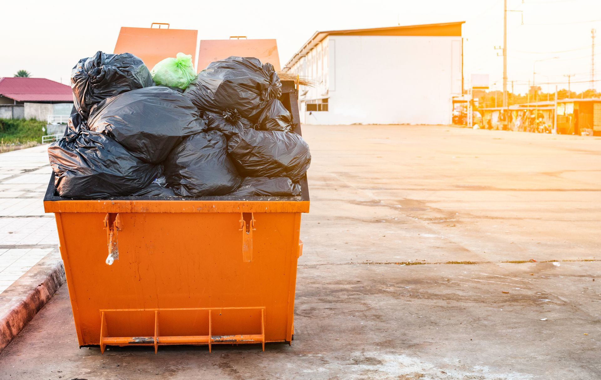 An orange dumpster filled with black garbage bags in a parking lot.