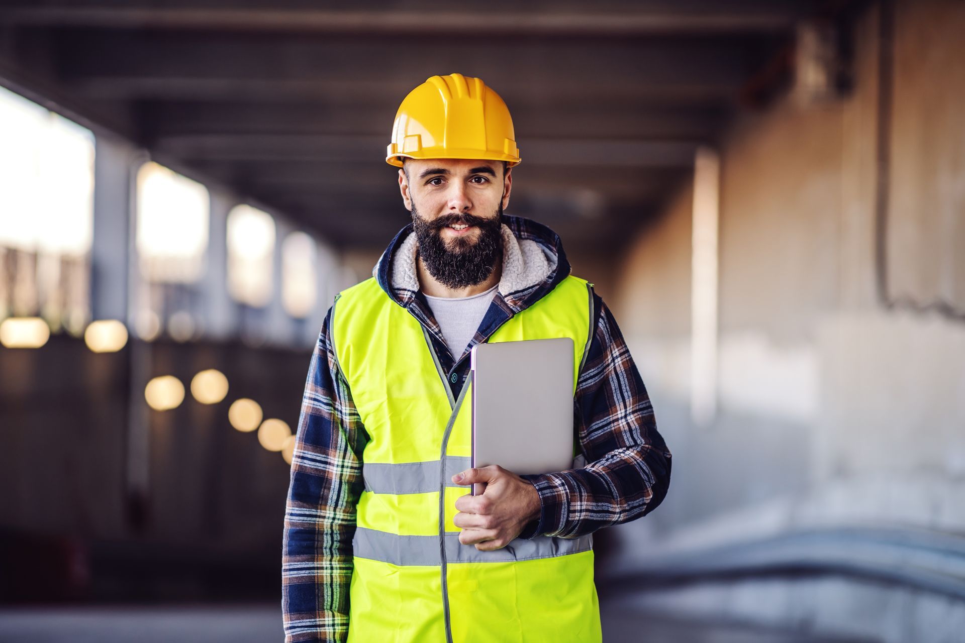 A construction worker wearing a hard hat and safety vest is holding a tablet computer.