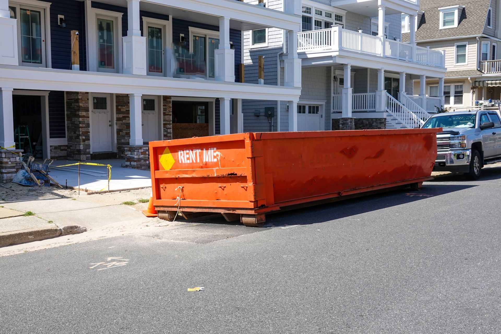 A large orange dumpster is parked on the side of the road in front of a house.