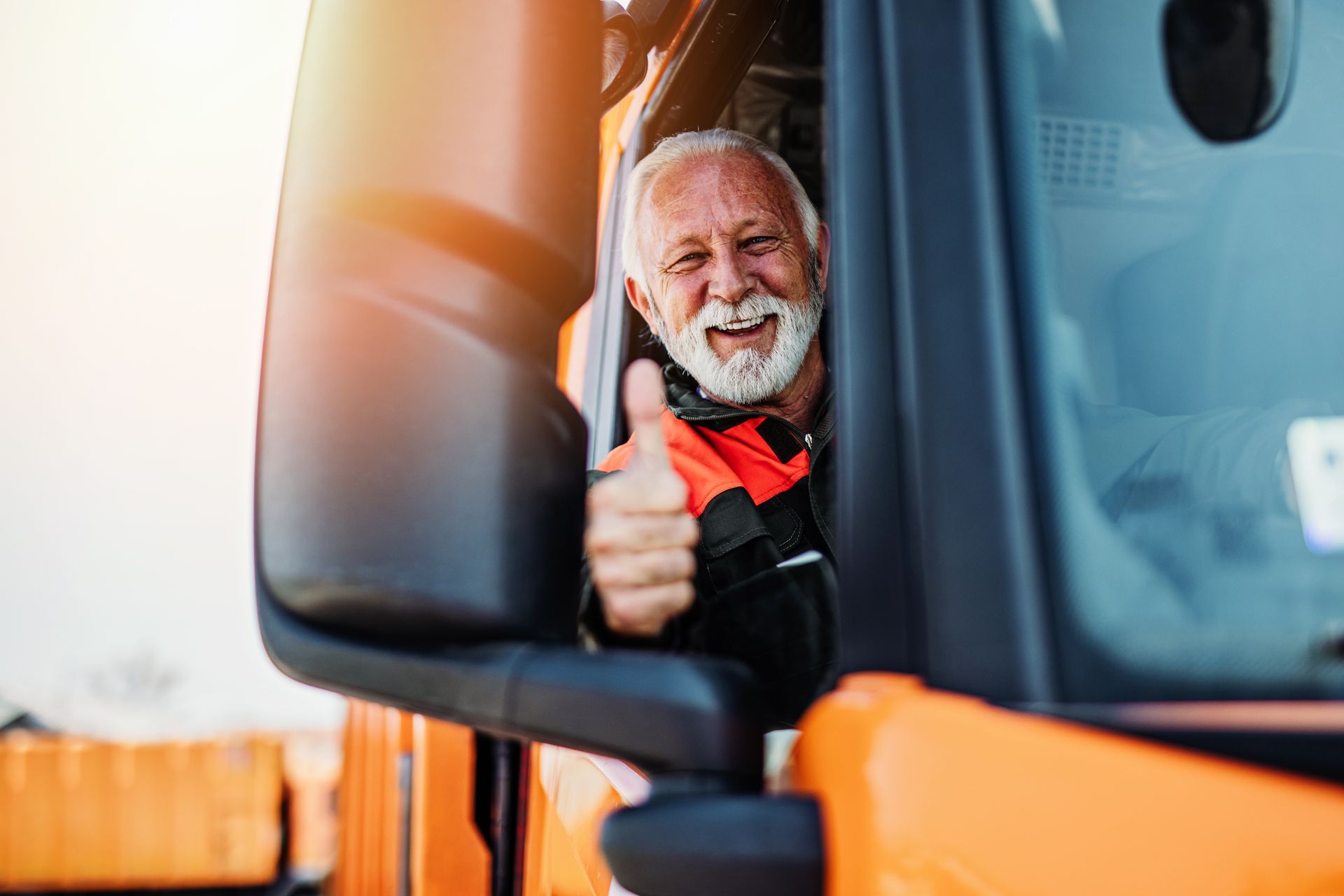 An older man is giving a thumbs up while sitting in the driver 's seat of a truck.