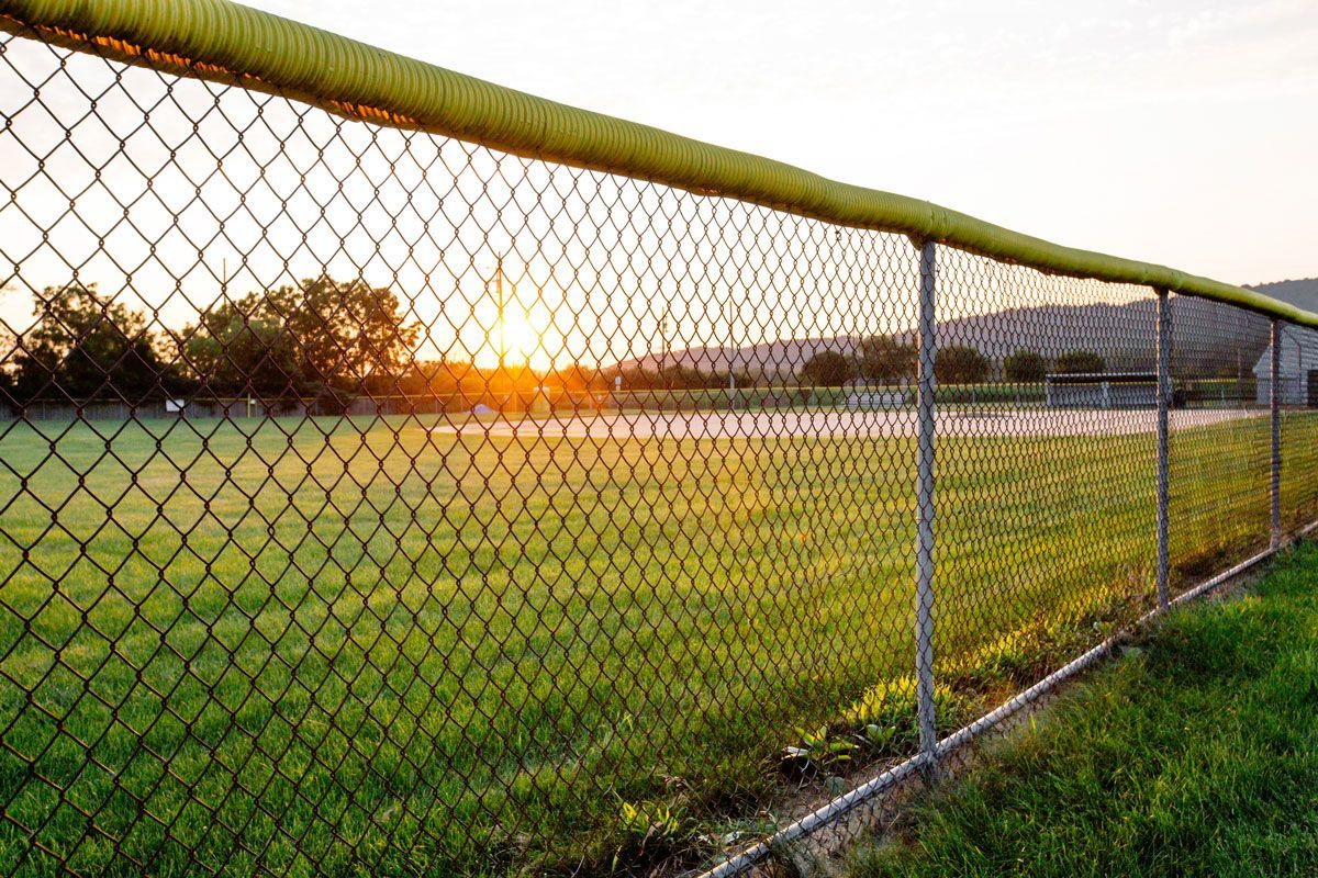 A chain link fence surrounds a baseball field at sunset.