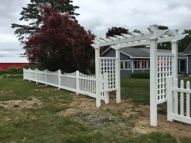 A white picket fence with a pergola in front of a house.