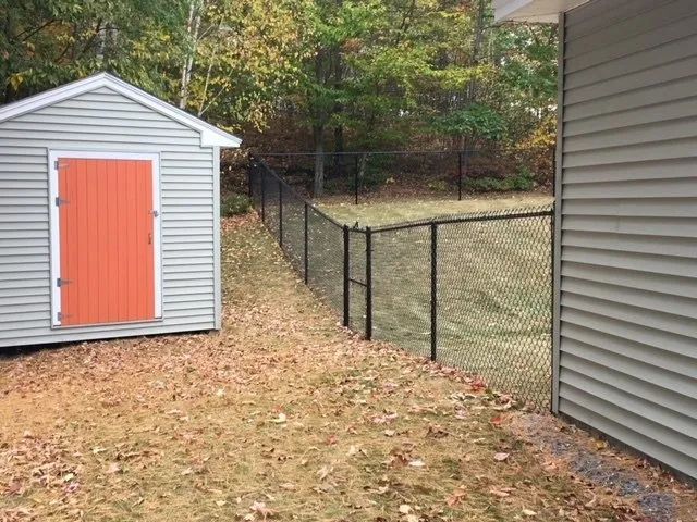 A shed with an orange door is next to a chain link fence.