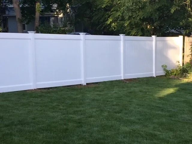 A white vinyl fence surrounds a lush green lawn in a backyard.