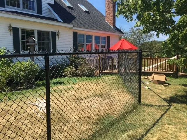 A chain link fence in front of a house with a red umbrella