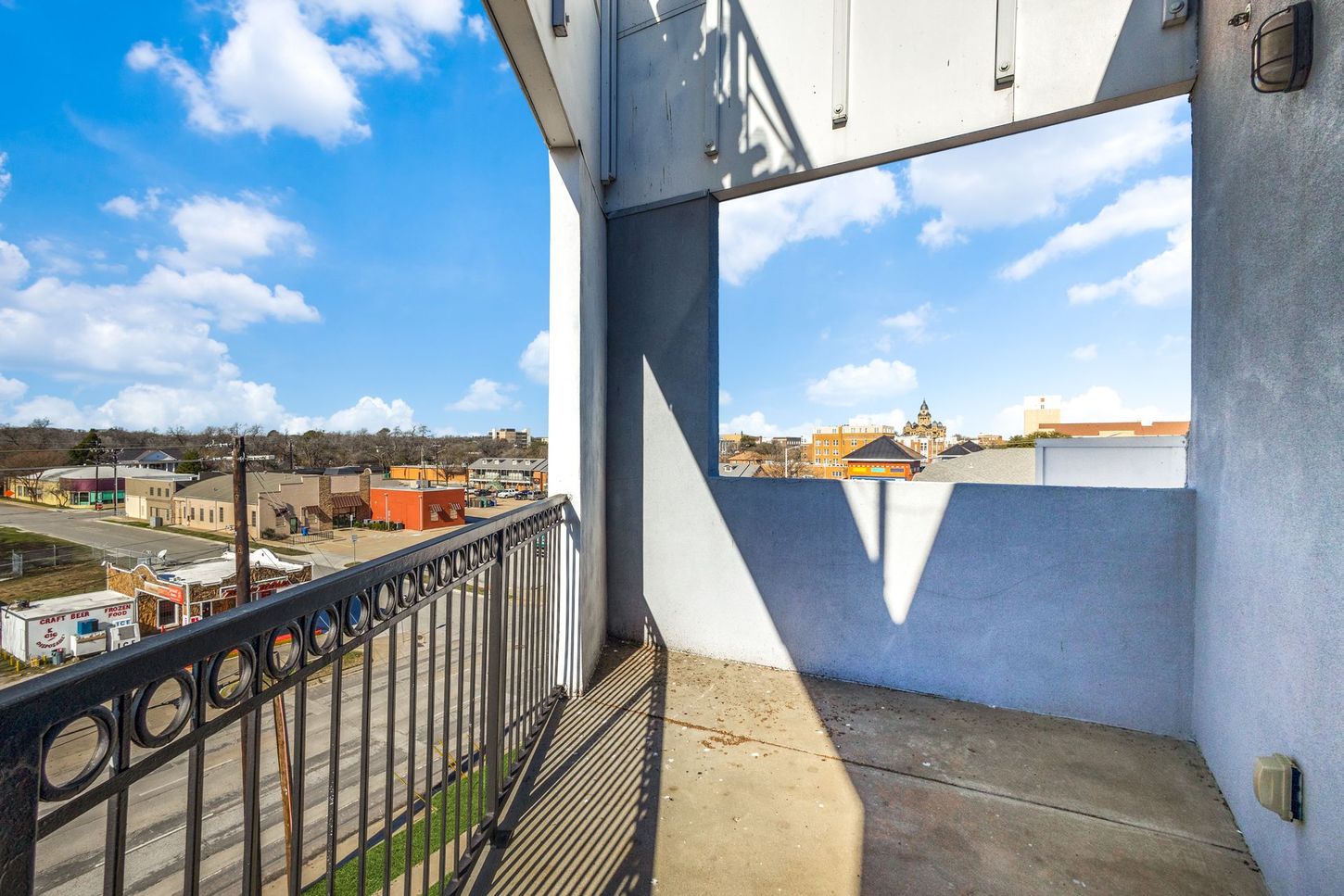 Balcony with wrought iron railing overlooking a town on a sunny day with clouds.