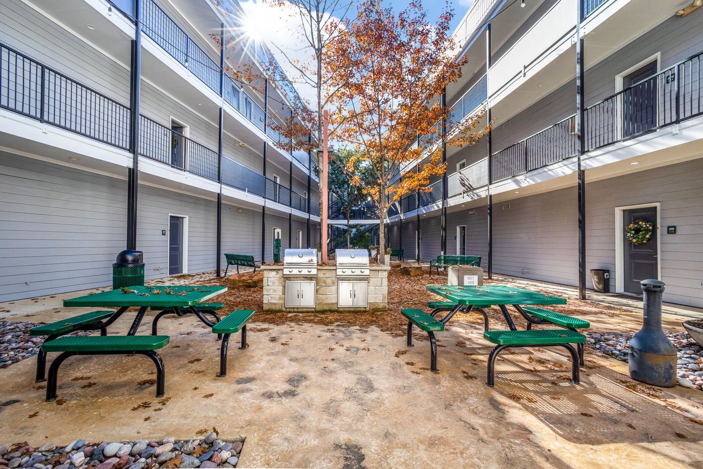 Courtyard with green picnic tables, grills, and a three-story building with black balconies.
