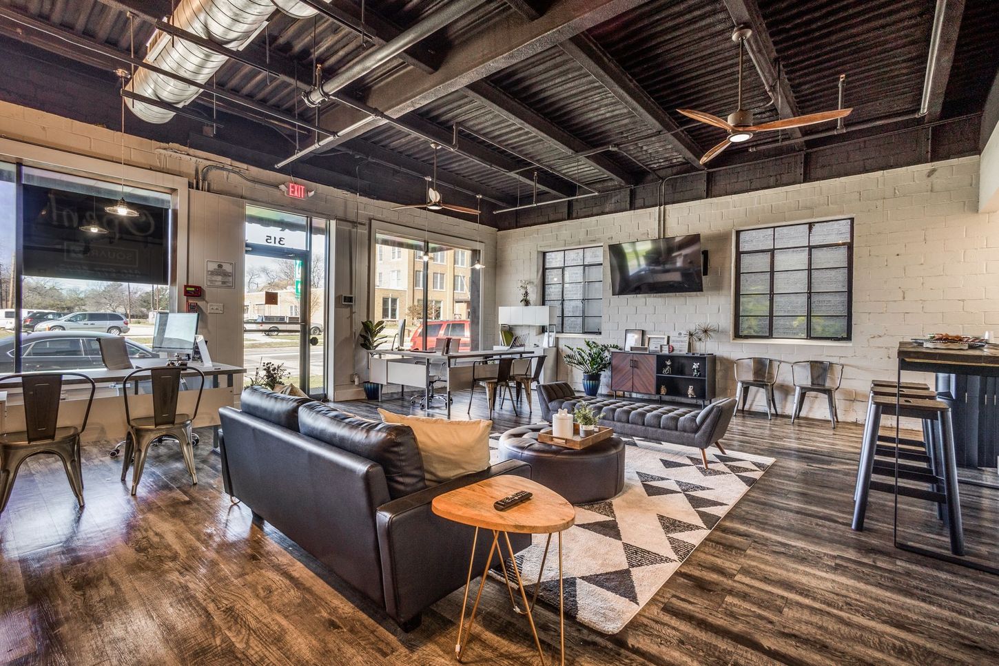 Modern office lounge with leather sofa, geometric rug, and industrial decor.