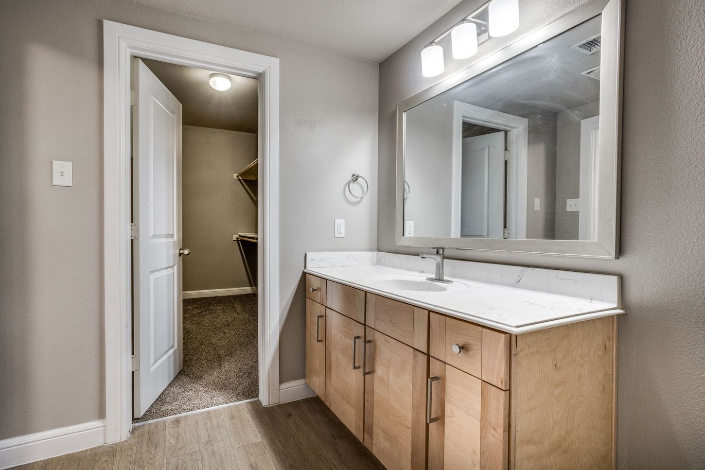 Bathroom with wood cabinets, white countertop, large mirror, and open door to a closet.