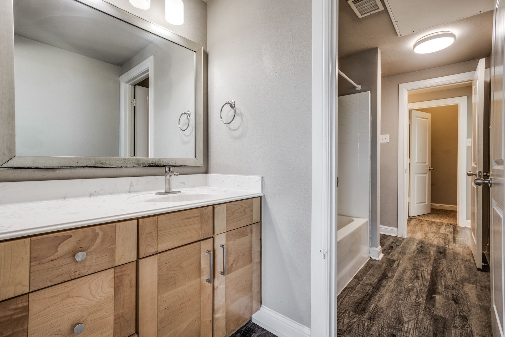 Bathroom with wood vanity, large mirror, and hallway with bathtub.