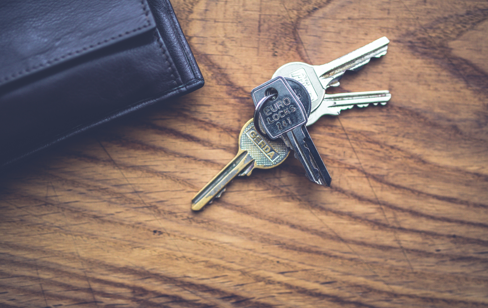 Wallet and three keys on a wooden surface.