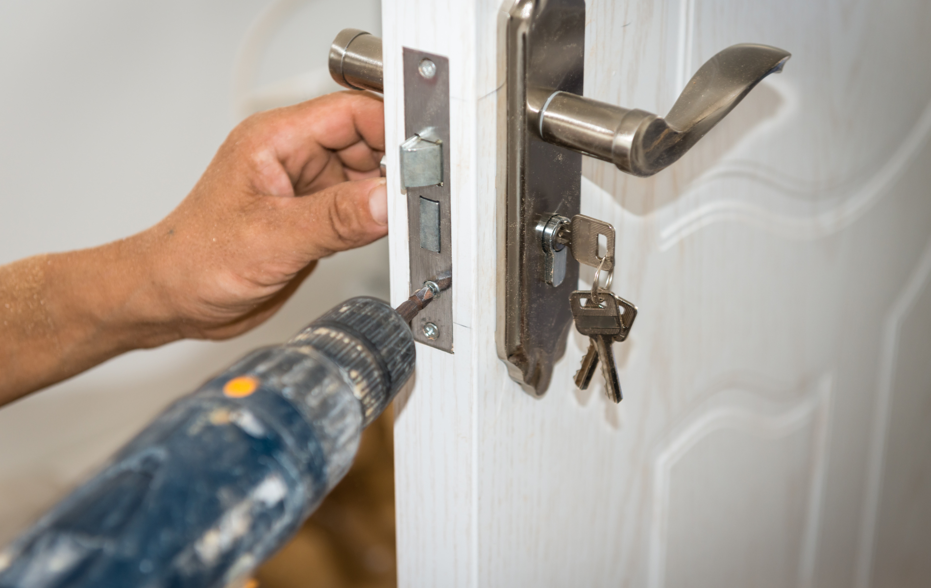 Person uses a power drill to install a door latch on a white door.