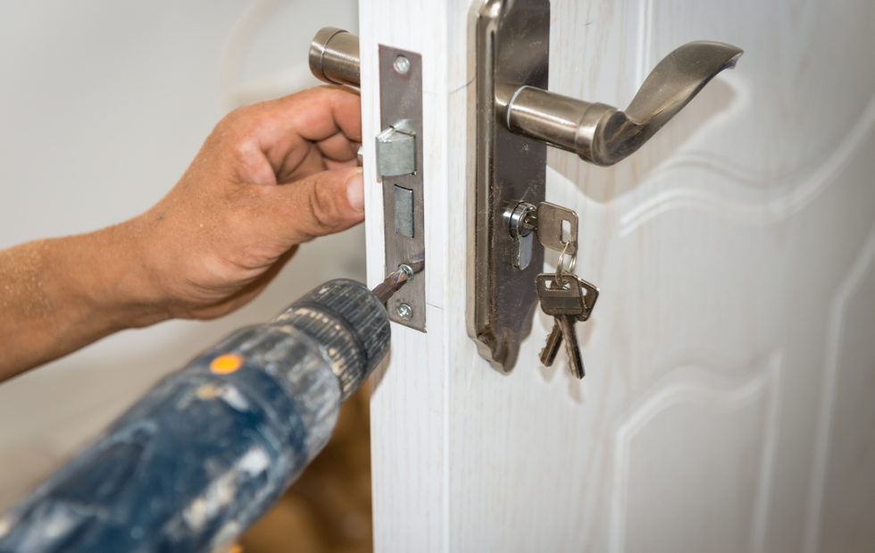 Person uses a power drill to install a door latch on a white door.