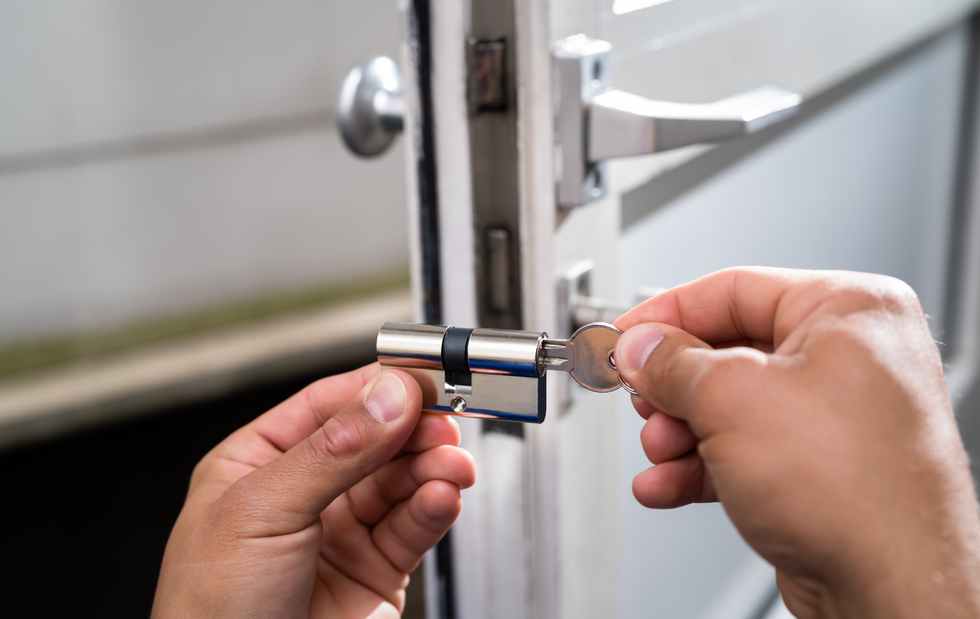 Hands inserting a key into a door lock cylinder, near a door handle.