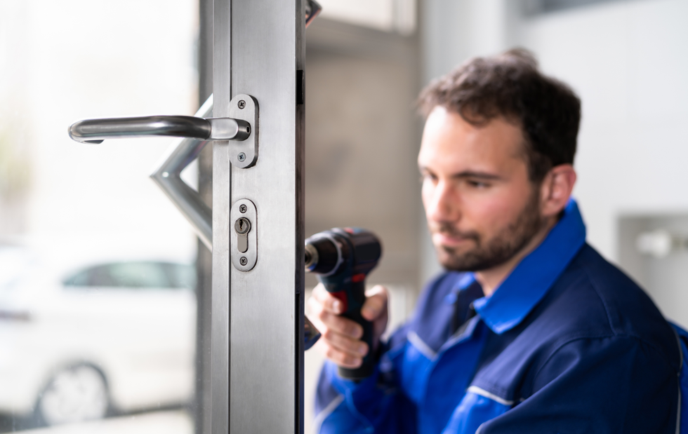 Man in blue overalls installing door lock with a power drill.