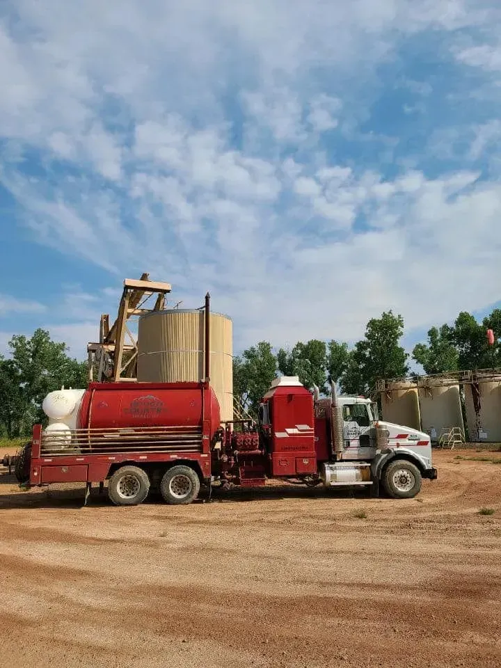 A red and white semi truck is parked in a dirt lot.