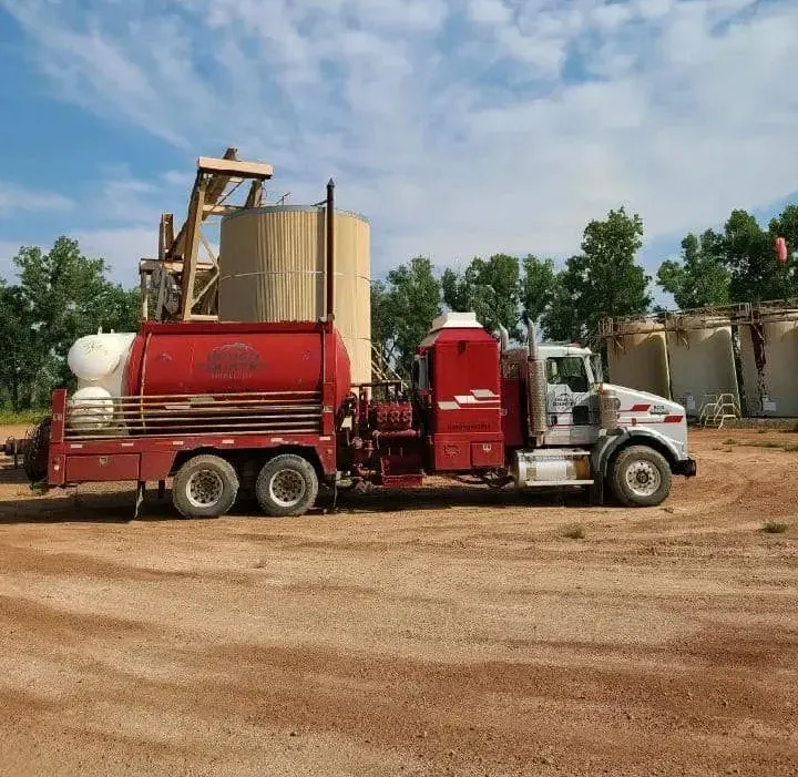 A red truck is parked in a dirt field
