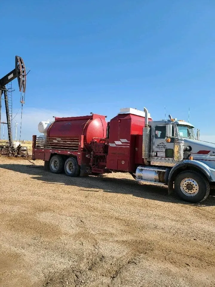 A red truck is parked in a dirt field next to an oil pump.