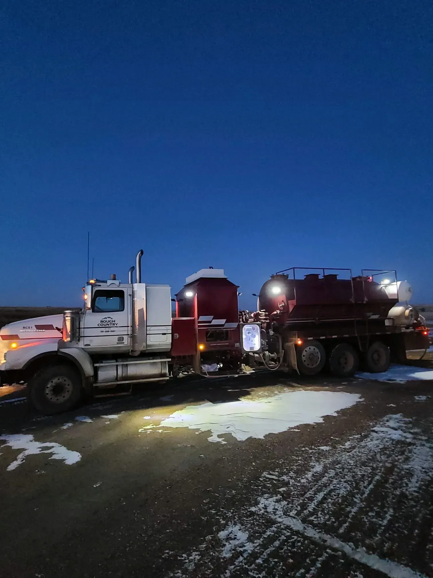 A semi truck is parked in a parking lot at night.
