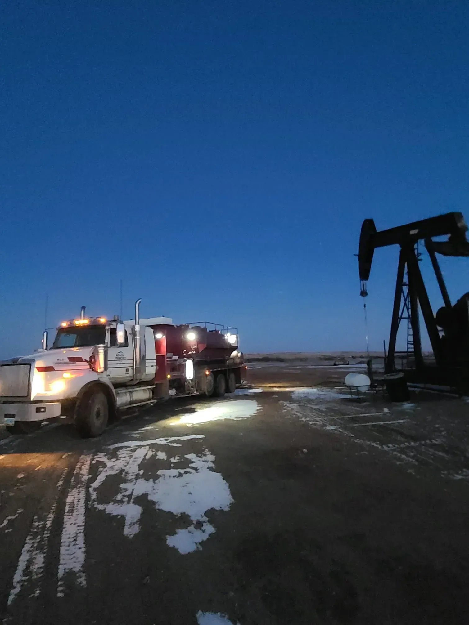 A semi truck is parked in front of an oil pump at night.