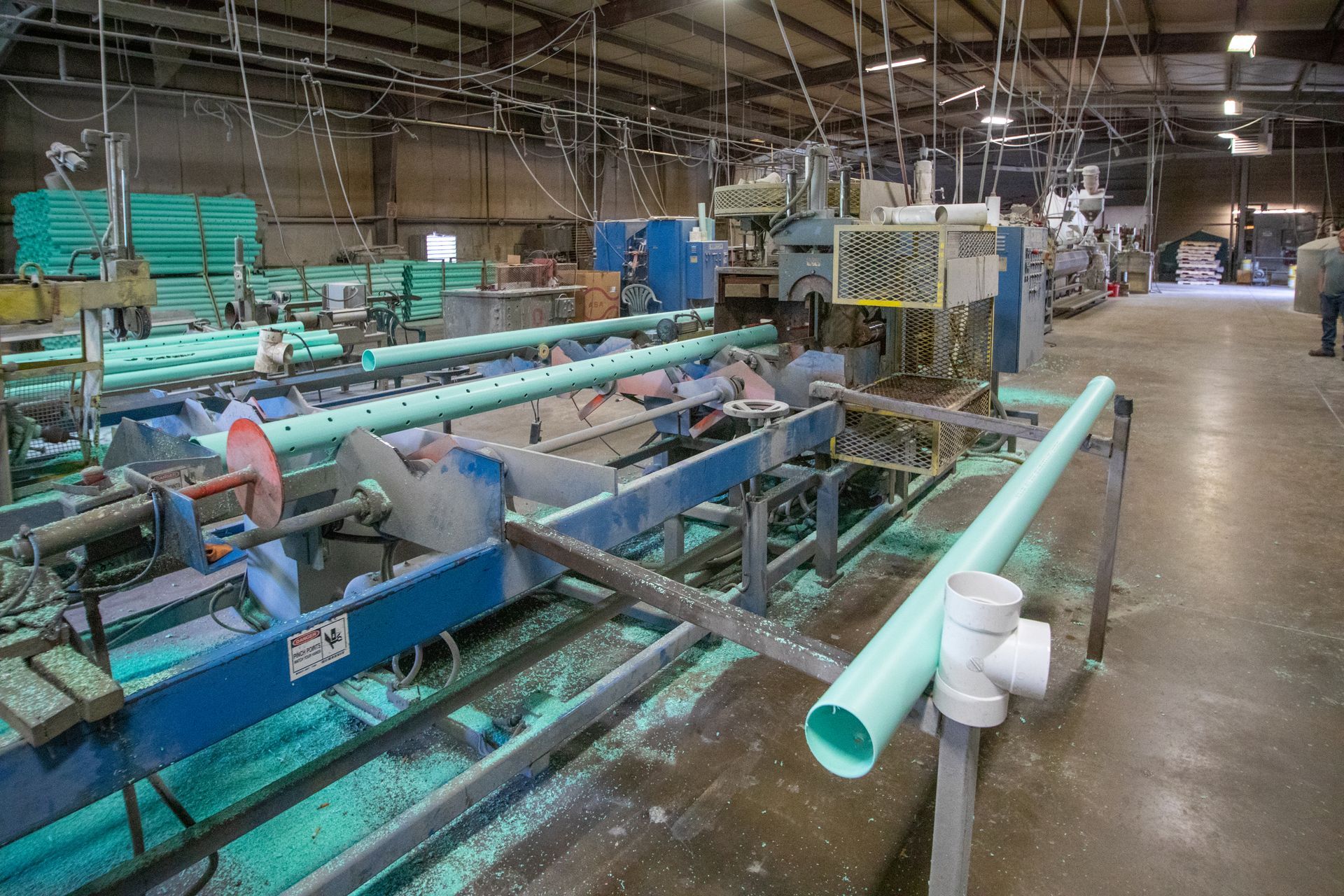 Factory floor with machinery cutting and assembling green PVC pipes.