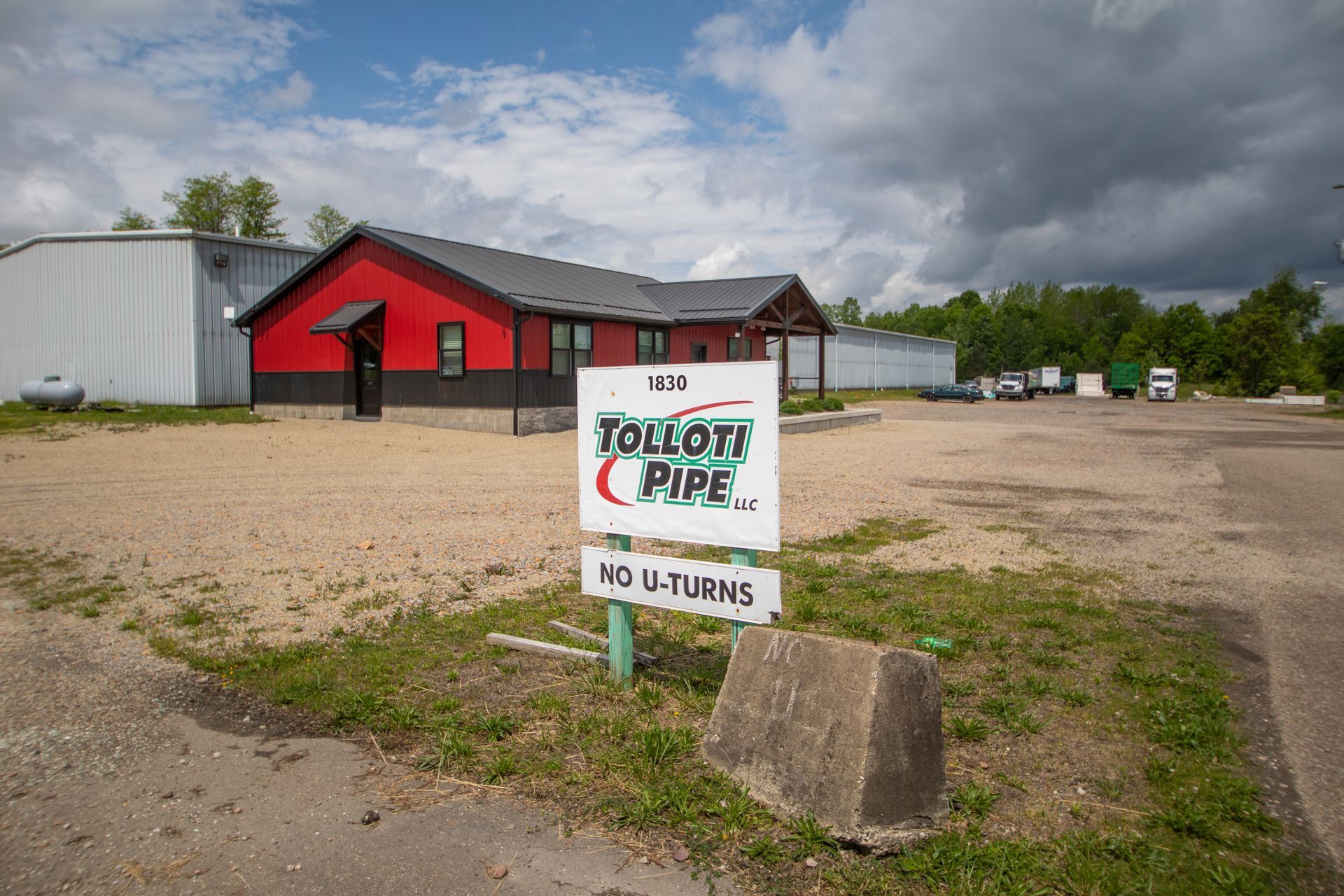 Exterior of Tolloff Pipe business; red building, white sign, gravel lot, cloudy sky.