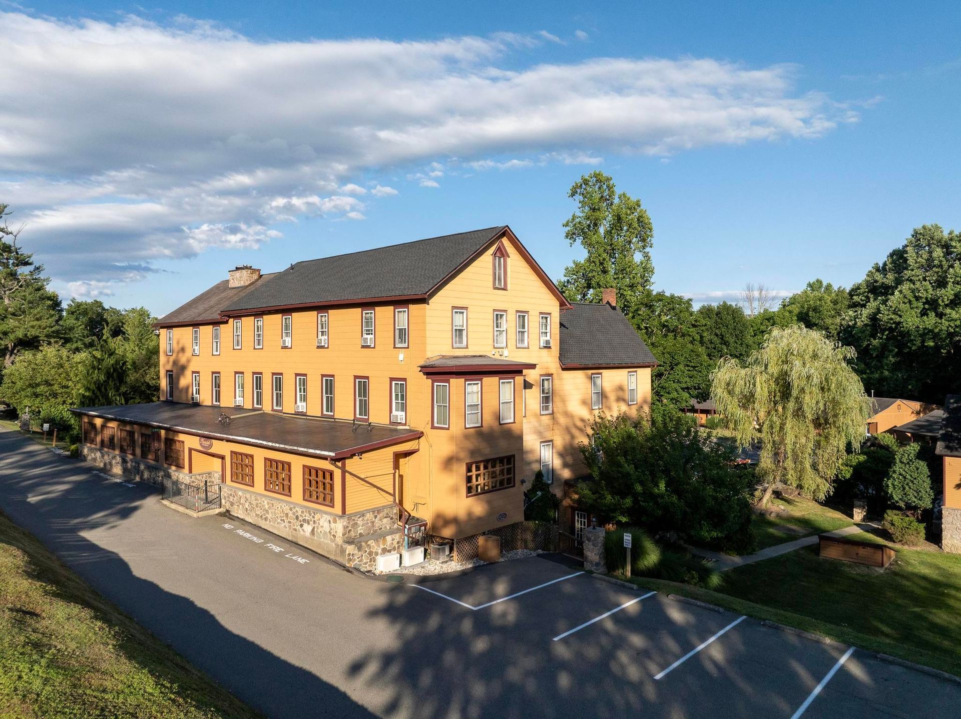 A large yellow building with a black roof is surrounded by trees and a parking lot.